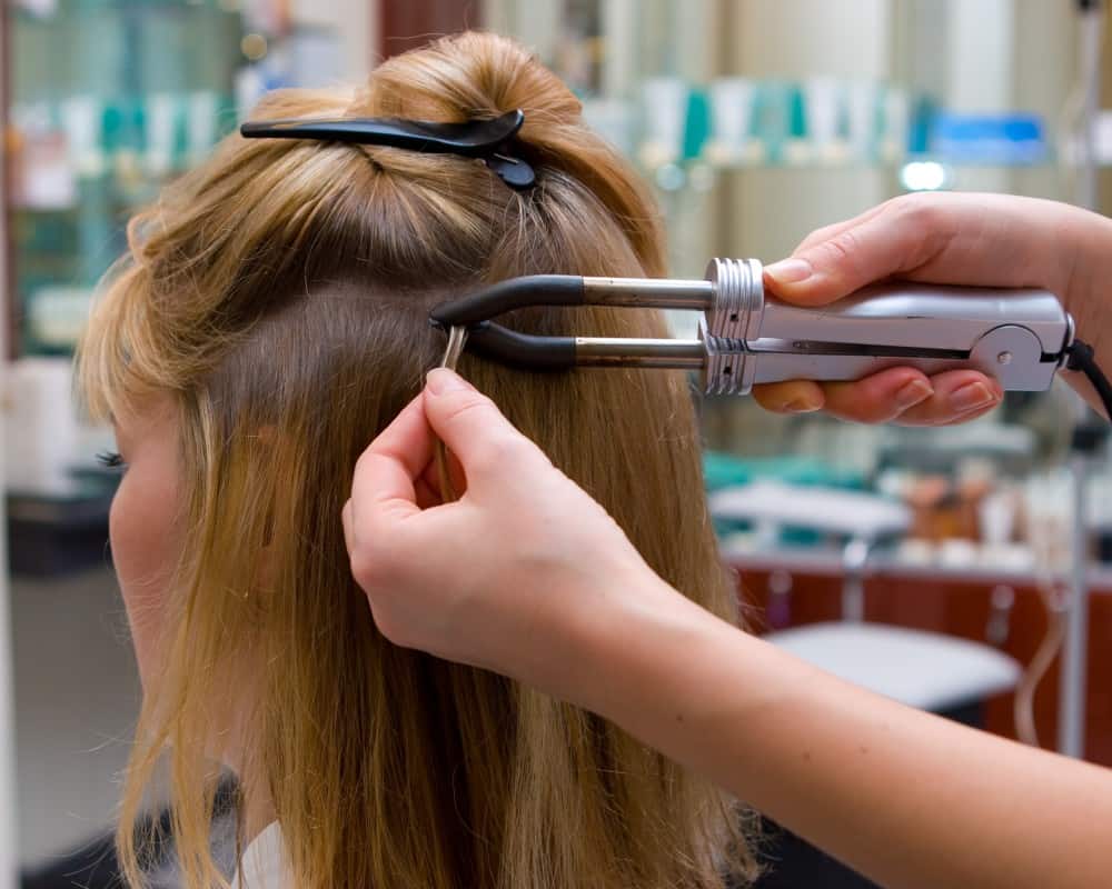 The hairdresser does hair extensions to a young girl, a blonde in a beauty salon. Professional hair care.