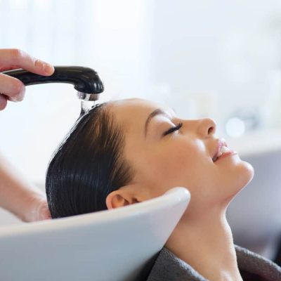 Beauty and people concept - happy young woman with hairdresser washing head at hair salon